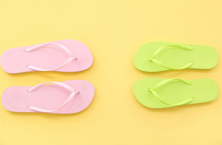 Blue sky with white clouds, sandy beach, and series of flip flops in many colors.